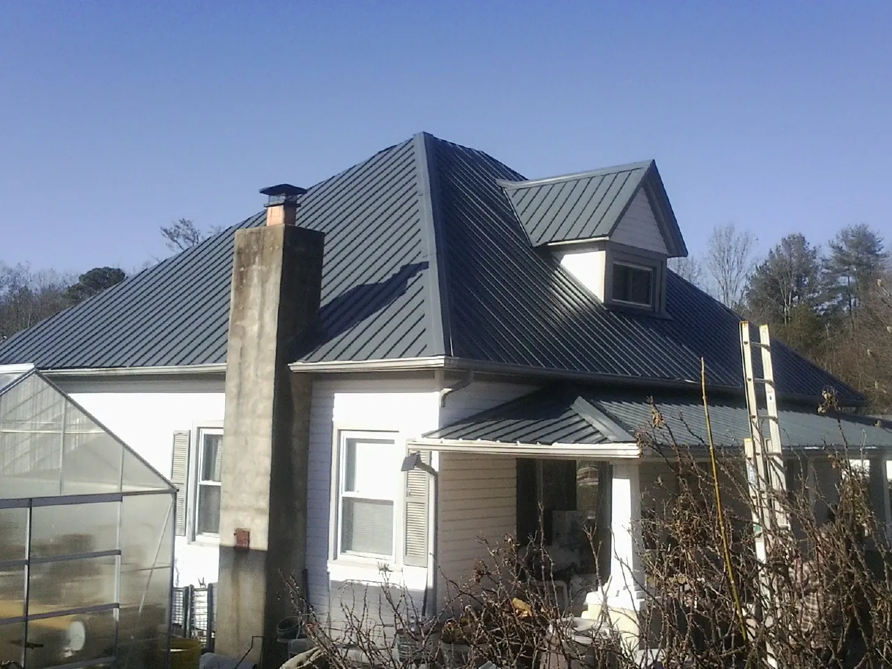 Dark blue standing seam metal roof on a white farmhouse with dormer — Slate & Tile Roof Repair by Roofing Brothers in Emigrant