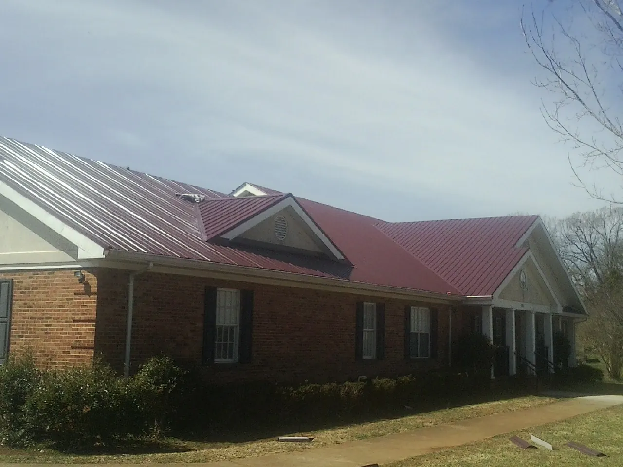 Red metal roof with gabled entries on a long brick building, from a Hail Damage Roof Repair job in Emigrant