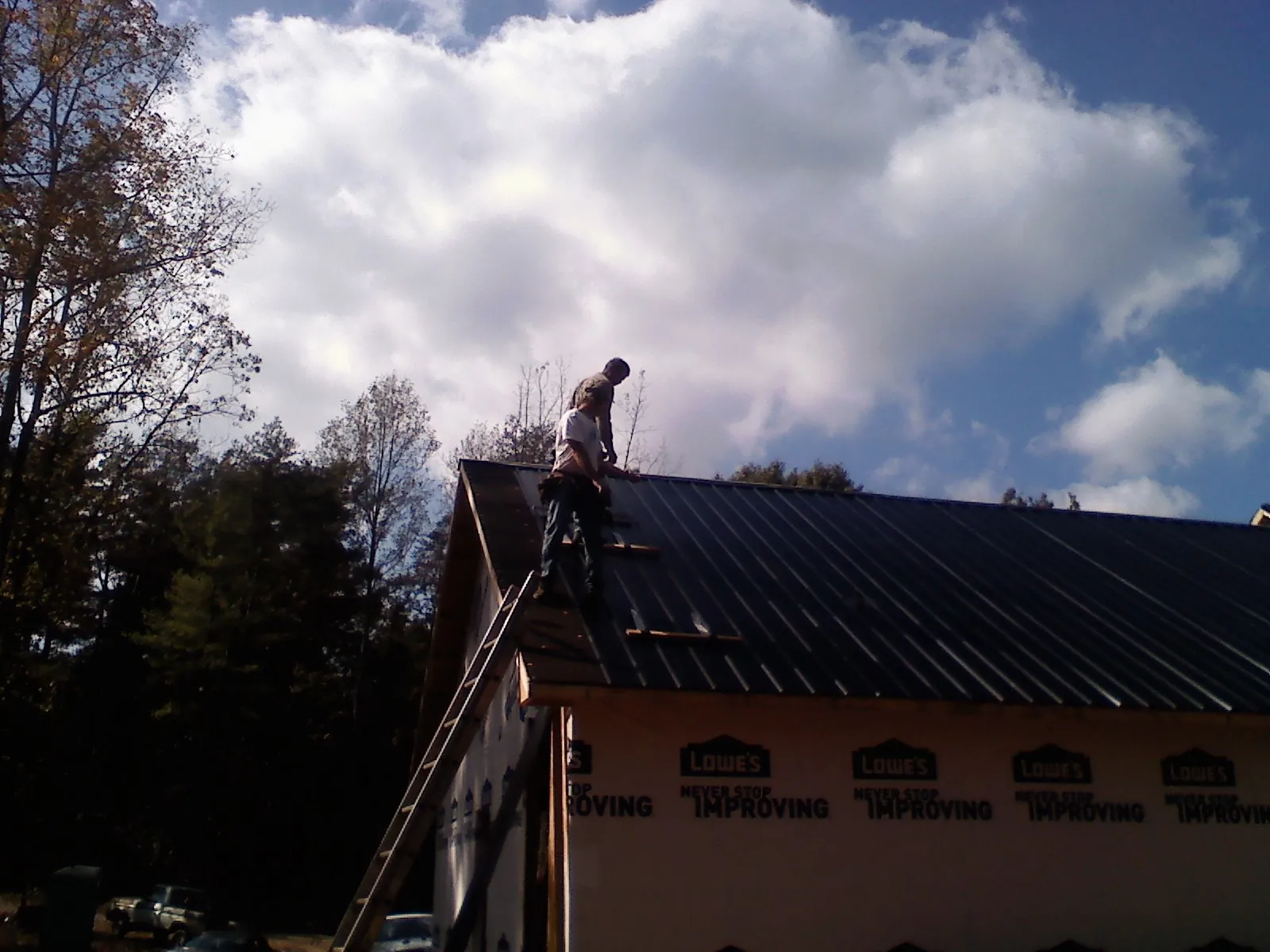 Roofer fastening dark metal panels high against a cloudy sky, from a Roof Inspection job in Emigrant